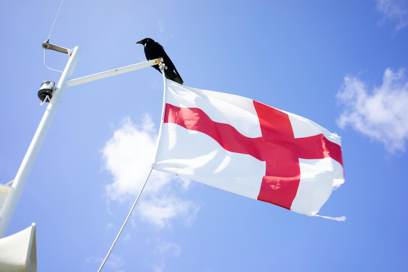 a English flag on a flagpole on a boat against a blue sky with soft clouds in the summer